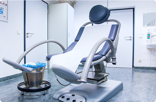 Seduta odontoiatrica moderna in sala visite: poltrona dentistica bianconera con braccioli, poggiatesta e lavandino in fondo, ambiente clinico sterile