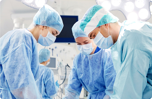 Equipe medica in sala operatoria, operatori in tute chirurgiche blu e mascherine durante un intervento.