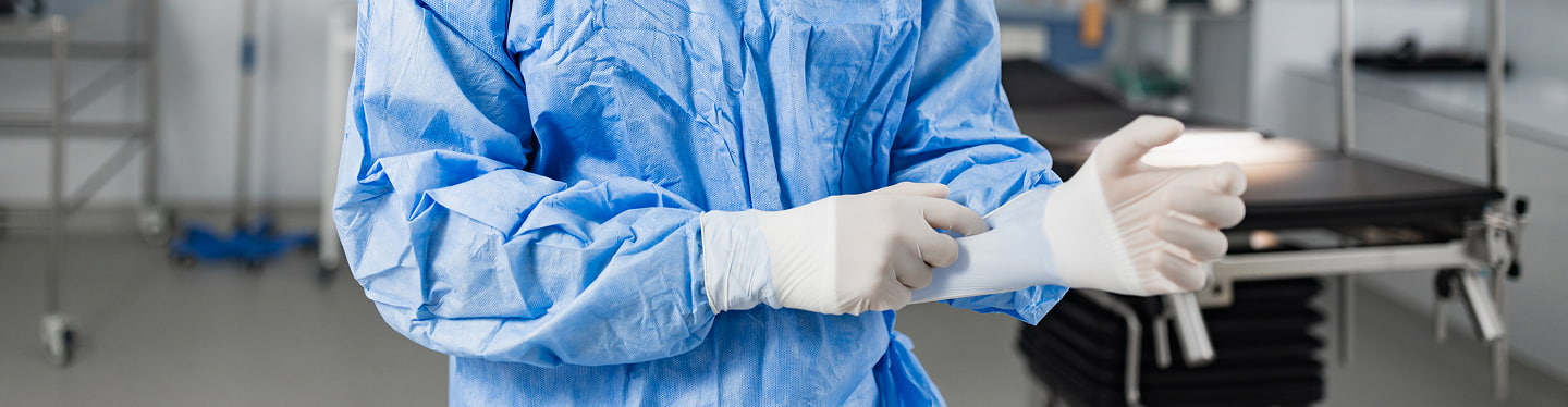 Operatore sanitario in camice blu usa guanti bianchi in un contesto clinico, attenzione e cura al paziente.