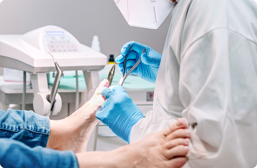 Operatore sanitario in guanti blu esegue una cura del piede su un paziente in una clinica con strumenti medici visibili sullo sfondo.