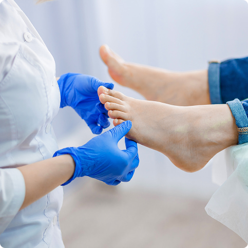 Trattamento medico: mani in guanti blu esaminano i piedi di una persona seduta.